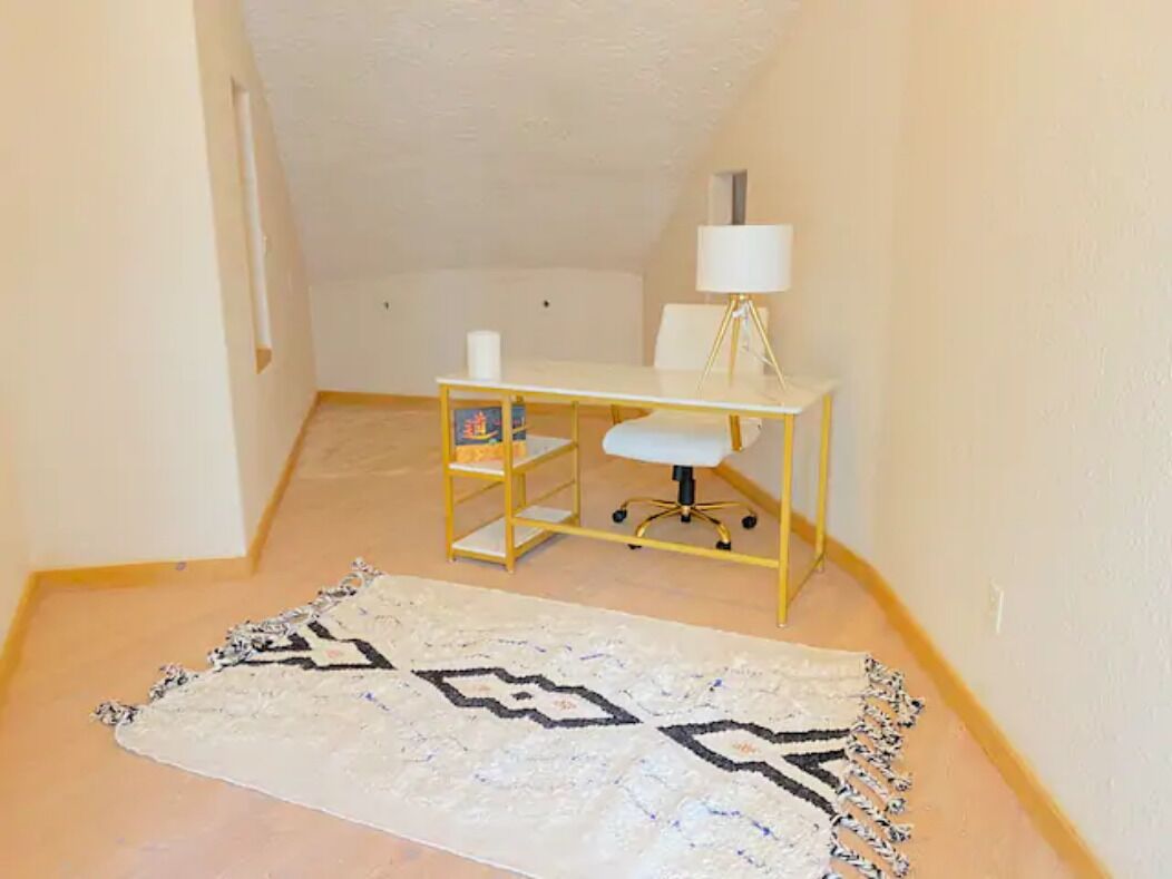Une petite pièce, bien rangée, avec un bureau, une chaise, une lampe et un tapis à motifs.
