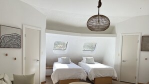 Et moderne soveværelse med to senge, et rundt træbord og en hængende lampe.