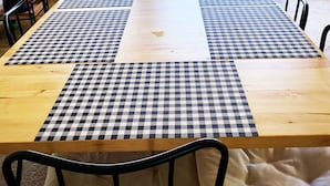 Una larga mesa de comedor con manteles a cuadros, sillas negras y un cartel con la palabra 'WELCOME' sobre las puertas.