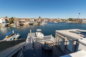 A marina with boats docked, a dining area with tables and chairs, and a view of houses along the water.