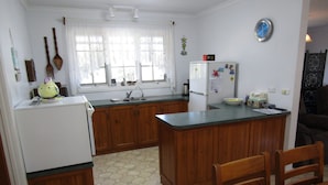 Cocina compacta con armarios de madera, un refrigerador blanco, un fregadero y un comedor con mesa y sillas de madera.