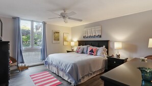 A bedroom with a bed, bedside lamps, a ceiling fan, a window with curtains, and artwork on the wall.