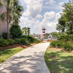 A pathway leading to a lighthouse, surrounded by lush greenery and a clear sky.
