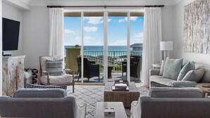 A spacious living room with a balcony overlooking the sea, furnished with modern sofas and chairs, a flat-screen TV, and a decorative cabinet. -  GULF FRONT on 30A with Beach setup! (Santa Rosa Beach)