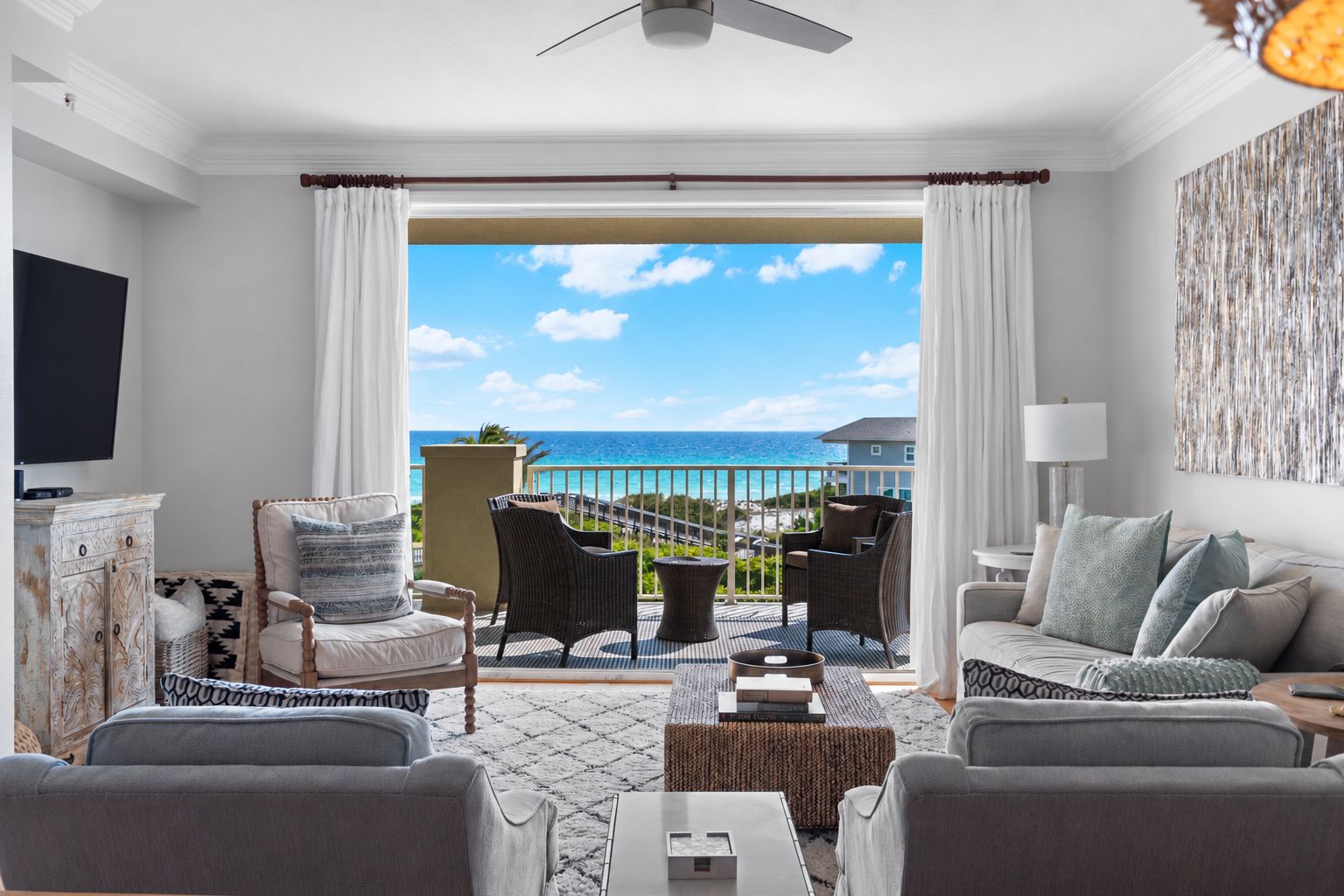 A modern living room with a view of the ocean, furnished with sofas, chairs, and a flat-screen TV.