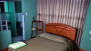 A bedroom with a bed, a wooden headboard, a small bedside table with a vase and a phone, and a curtain. - Hospedaje Don Juan (Cusco)