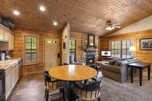 Cozy cabin interior with a central dining table, comfortable sofa, and fireplace.