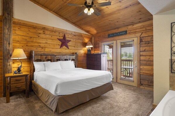Relax in this serene bedroom with a large bed, wooden ceiling fan, and a door leading to an outdoor area with a view of lush greenery.