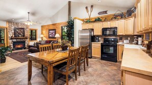 A spacious kitchen with wooden cabinets, a stone fireplace, and a dining area with a wooden table and chairs. - Lovely Log Cabin with Whirlpool Tub in Branson Theatre District (Branson)