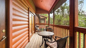 A wooden deck with a round table and chairs, a view of the surrounding trees, and a wooden door. - Lovely Log Cabin with Whirlpool Tub in Branson Theatre District (Branson)
