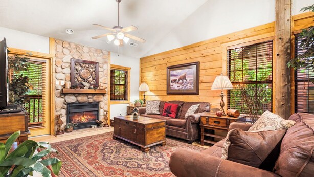 A cozy living room with a fireplace, wooden walls, a large brown leather sofa, and a patterned rug. - Lovely Log Cabin with Whirlpool Tub in Branson Theatre District (Branson)