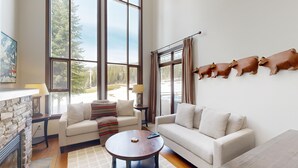 A spacious living room with large windows, a stone fireplace, and a wall-mounted animal sculpture. - Dog-friendly, 3 bedroom ski-in/ski-out end unit (Sun Peaks)