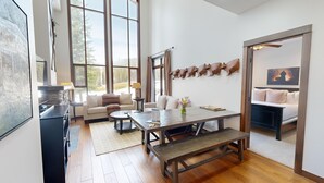 A spacious living room with a large window, a sofa, a coffee table, and a dining table. - Dog-friendly, 3 bedroom ski-in/ski-out end unit (Sun Peaks)