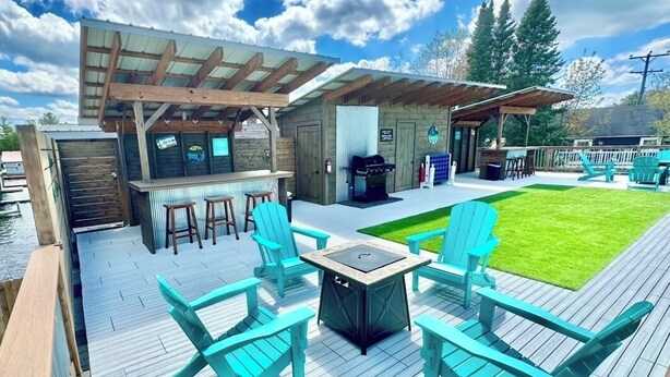 A deck with outdoor seating, a grill, and a covered area with a bar. - Torch Lake Sandbar Directly Across the Street With Indoor Boat Slip Unit A (Rapid City)