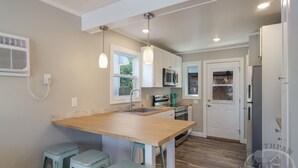 A modern kitchen with a wooden island, white cabinets, a microwave, and a refrigerator. - Torch Lake Sandbar Directly Across the Street With Indoor Boat Slip Unit A (Rapid City)