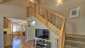 A spacious living area with a wooden staircase, a flat-screen TV on a stand, and a dining area with chairs and a table. - Forest-View Retreat in Payson, Close to Hiking! (Payson)