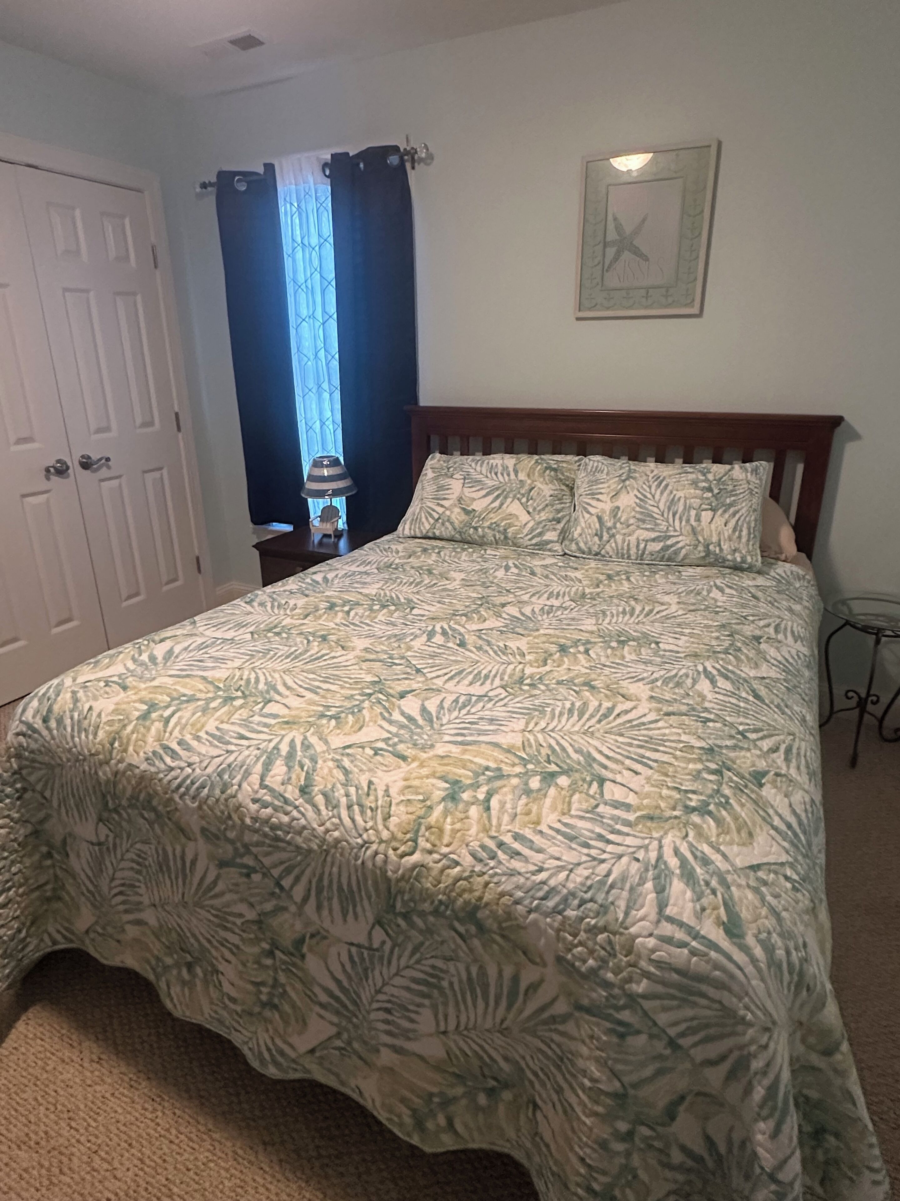 A bedroom with a bed, a nightstand, a lamp, a door, and a window with curtains.