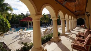 An outdoor patio area with columns, seating, and a pool. - Warmth and harmony await you. (Bonita Springs)