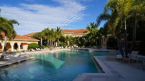 A swimming pool with lounge chairs and palm trees, surrounded by a building with a red-tiled roof. - Warmth and harmony await you. (Bonita Springs)