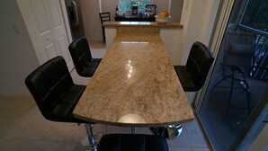 A kitchen with a granite countertop, four black chairs, and a window with a view of greenery. - Warmth and harmony await you. (Bonita Springs)