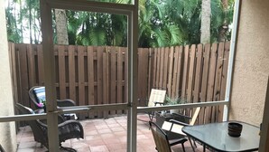 Un patio con cerramiento de madera, mobiliario exterior y una puerta de cristal que da a un porche con baldosas.
