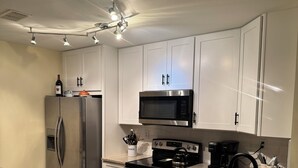 Una cocina moderna con armarios blancos, electrodomésticos de acero inoxidable, encimera de granito y ventilador de techo.