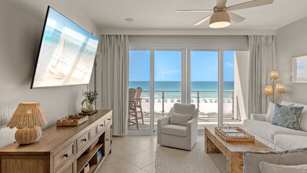 Una sala de estar con televisor, ventilador de techo, sofá, mesa de centro y vista a la playa.