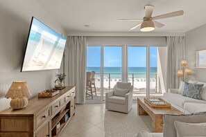 Ein Wohnzimmer mit Fernseher, Deckenventilator, Sofa, Couchtisch und Blick auf den Strand.