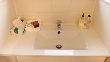 Un bagno con un lavandino bianco, una scatola di fazzoletti e due flaconi di prodotti per la cura dei capelli.