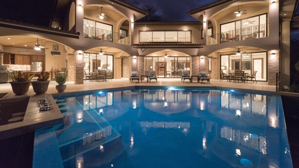 Une grande maison à deux étages, dotée d’une piscine, de mobilier d’extérieur et d’un balcon bien éclairé.
