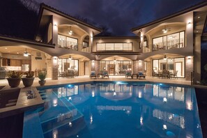 Une grande maison à deux étages, dotée d’une piscine, de mobilier d’extérieur et d’un balcon bien éclairé.
