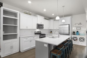 A modern kitchen with white cabinetry, a central island with bar stools, stainless steel appliances, and pendant lighting.