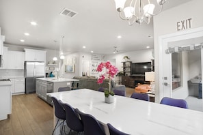 A modern kitchen with white cabinets, a stainless steel refrigerator, and a dining area with a marble table and purple chairs.