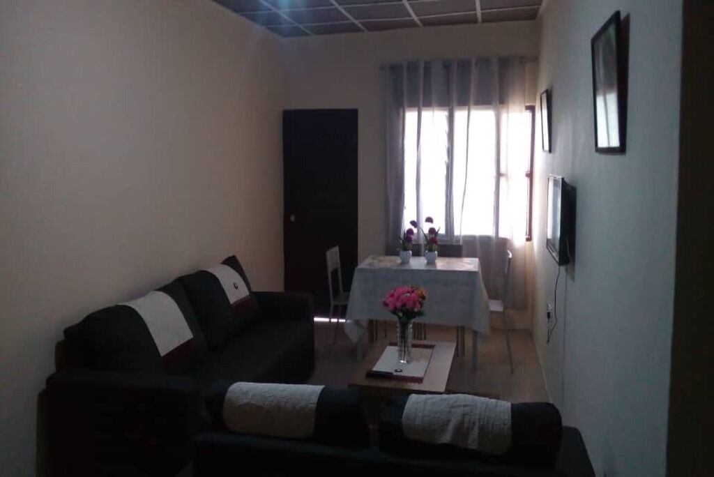 A living room with a sofa, a dining table with chairs, and a TV mounted on the wall.