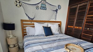 A bedroom with a bed, a wooden headboard, a wall-mounted air conditioner, a small bedside table with a lamp, and a wooden wardrobe. - VistaPinero Beach Front Apartment - Joyudas Cabo Rojo (Cabo Rojo)