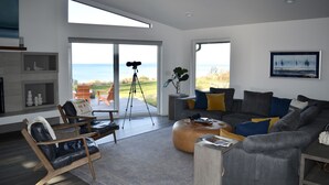 Un salon moderne avec une grande fenêtre, un canapé gris, une table basse en bois et un fauteuil en cuir.