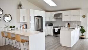 Une cuisine moderne avec des meubles blancs, des appareils en acier inoxydable et un îlot central doté de tabourets de bar.