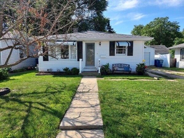 A single-story house with a front porch, a small garden, and a pathway leading to the door.