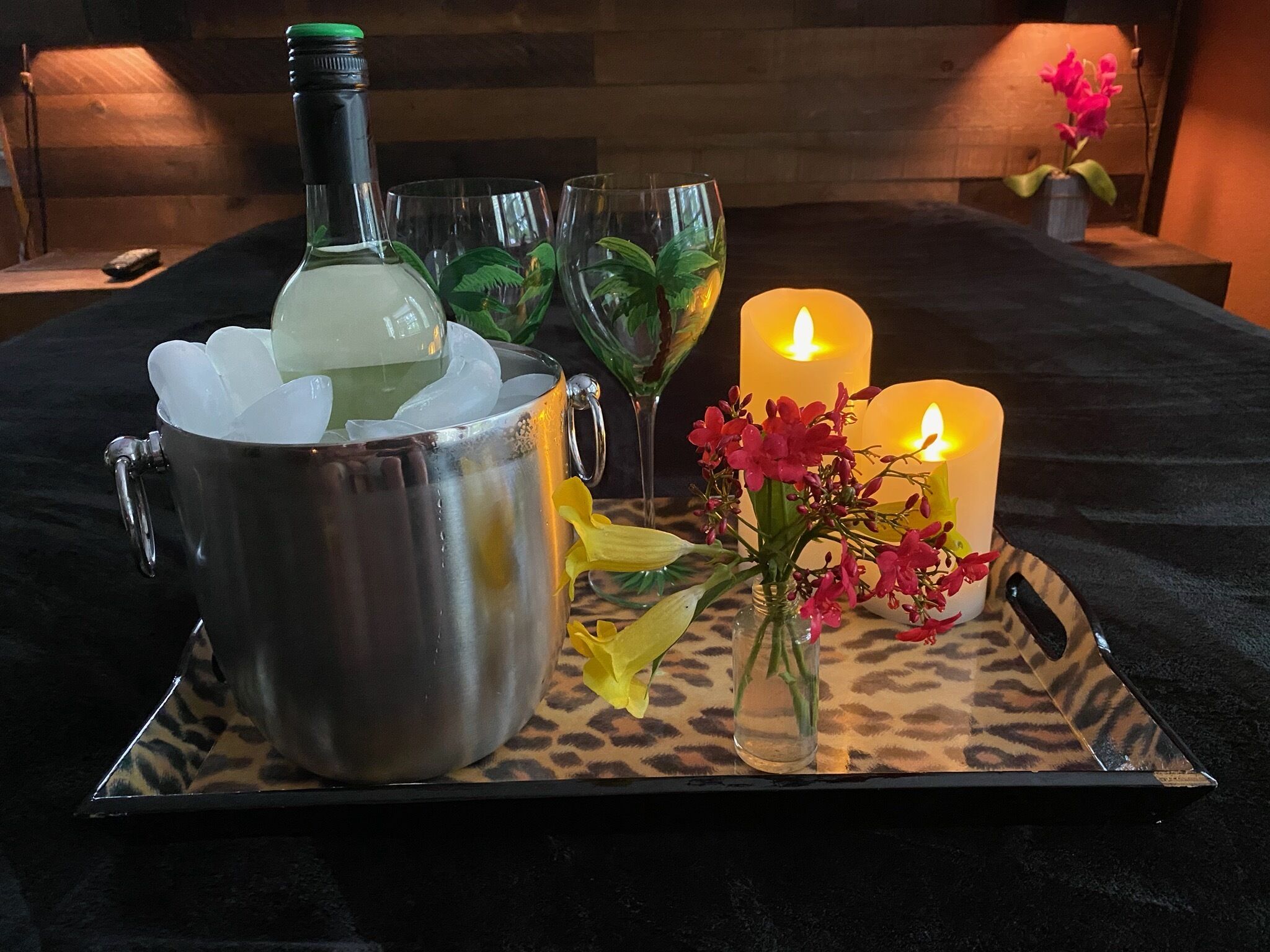 Een dienblad met een metalen beker gevuld met ijs, een fles, twee brandende kaarsen en een vaas met bloemen.