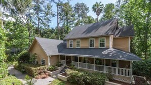 A two-story house with a porch, surrounded by lush greenery and trees. -  Private Studio Entry (Ponte Vedra Beach)