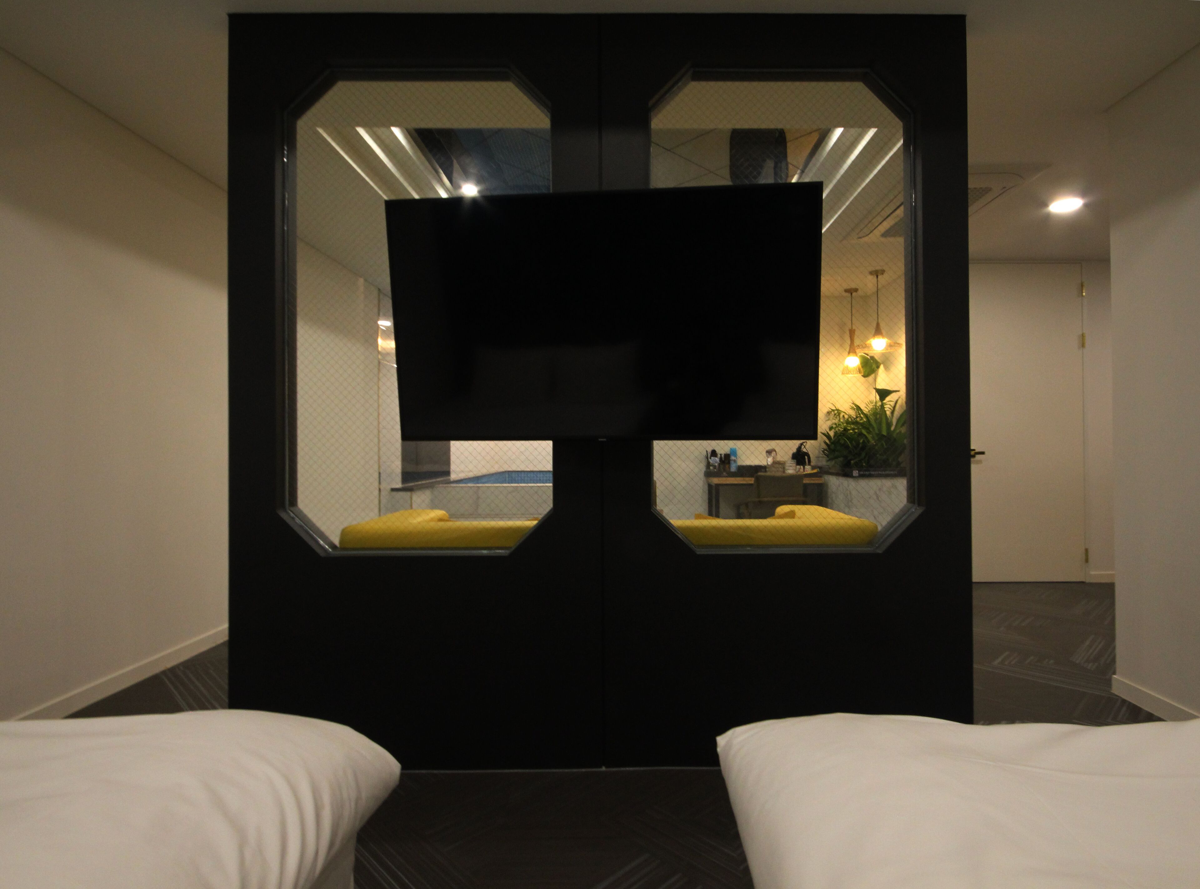 Ein Hotelzimmer mit einem großen Spiegel, zwei Betten, einem Fernseher und einem kleinen Schreibtisch mit Stuhl.