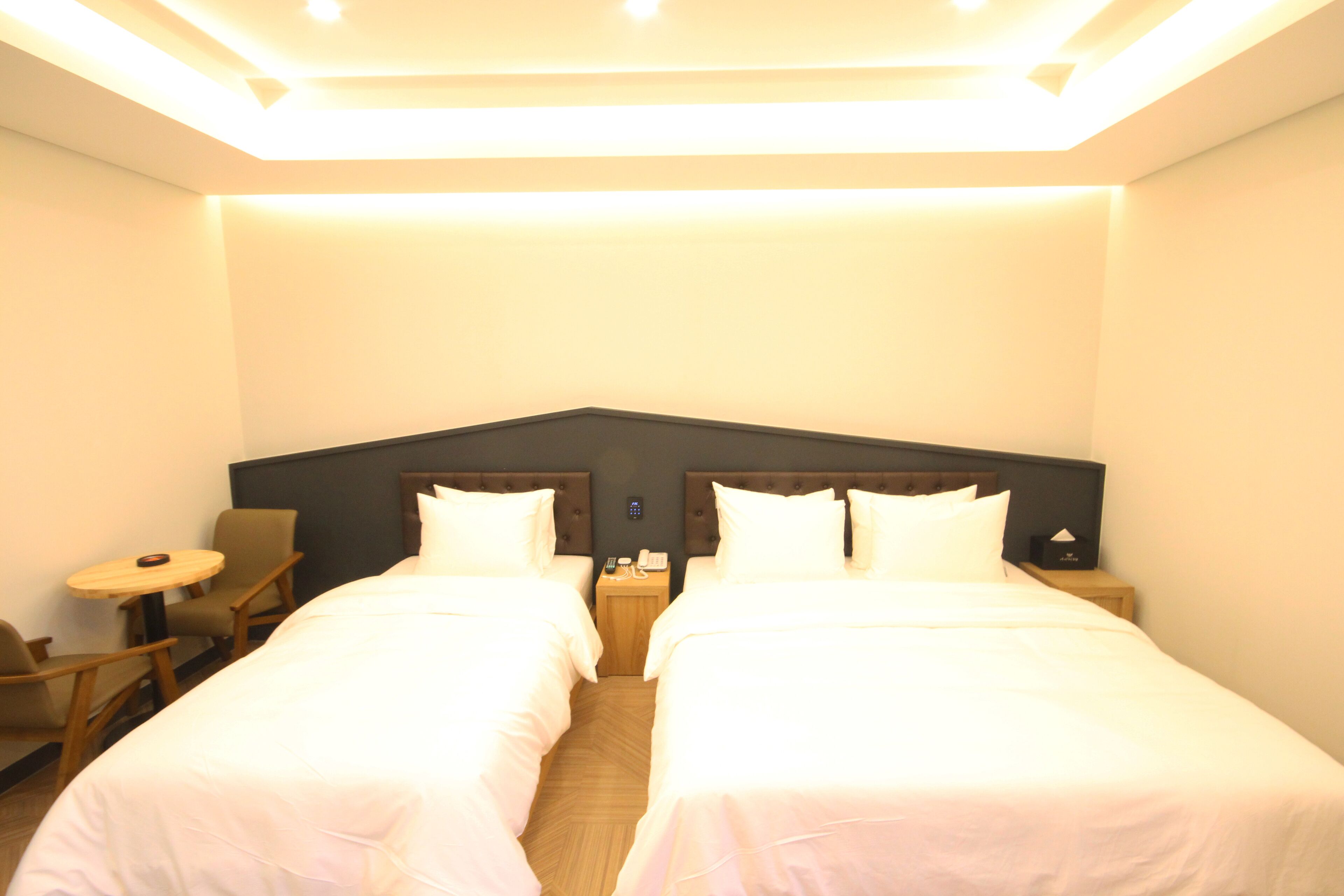 A hotel room with two beds, a small table, and a chair.