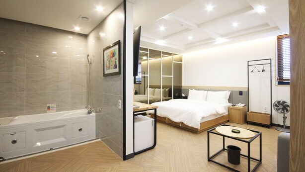 A modern hotel room with a large bed, a separate bathroom with a bathtub, a small table, and a fan. - Amare Hotel (Daegu)