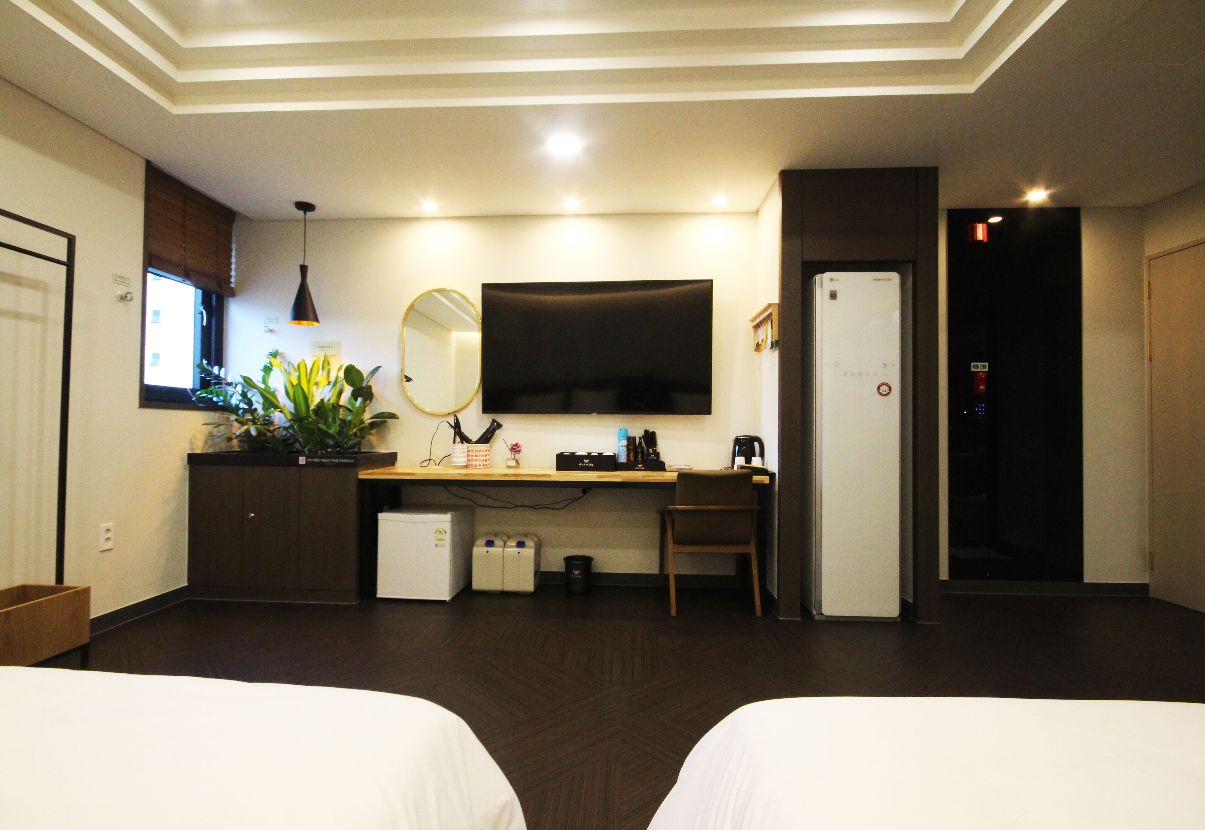 A hotel room with two beds, a desk with a computer, a television, and a refrigerator.
