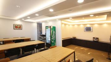 A modern dining area with wooden tables and chairs, a refrigerator, and a counter with a coffee machine.