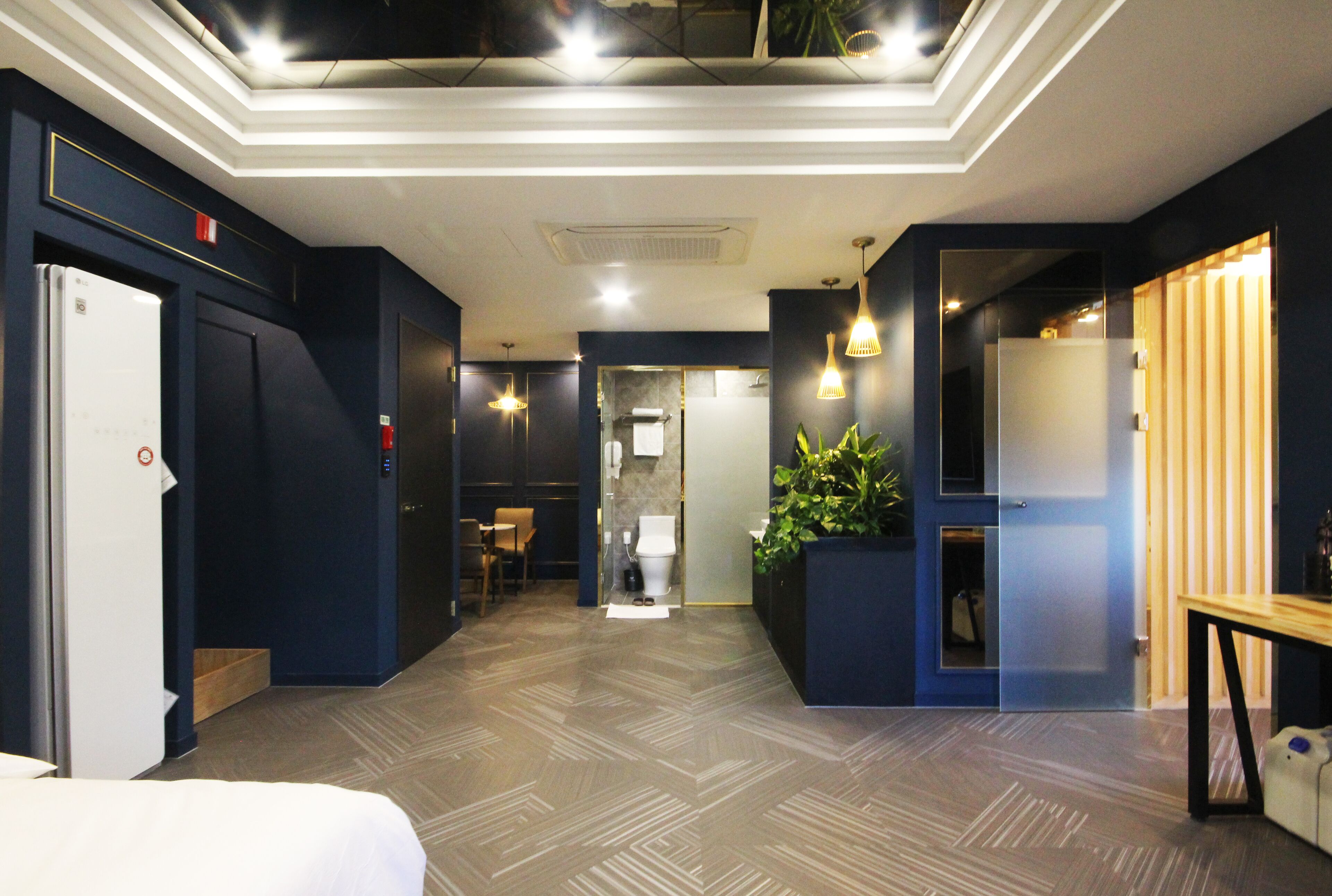 A hotel lobby with a modern design, featuring a reception desk, a seating area, and a large potted plant.