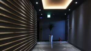 A modern hallway with a reflective floor, a potted plant, and a fire extinguisher. - Amare Hotel (Daegu)