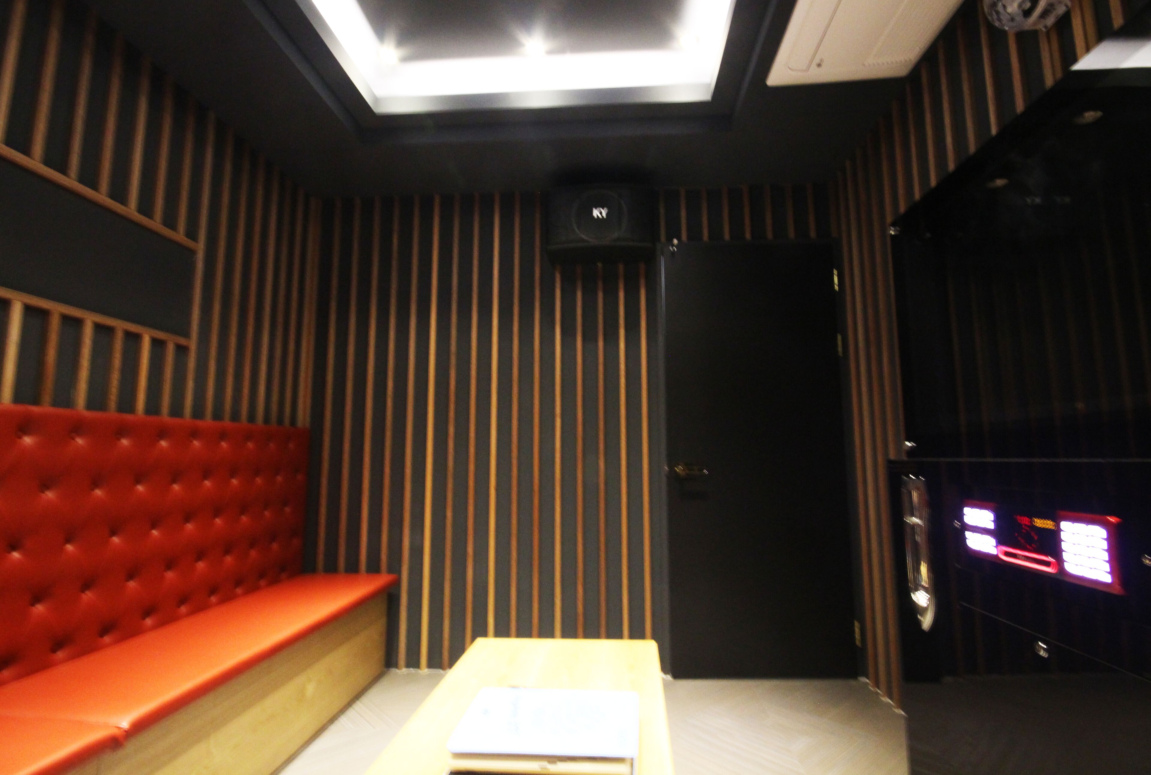 Una habitación con un banco tapizado en rojo, una mesa de madera y una puerta con un panel negro.