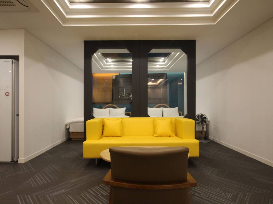 Un hall d’entrée moderne avec un canapé jaune, un pouf marron et un plafond doté d’un éclairage encastré.