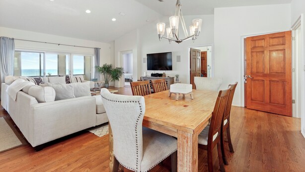 Amplia sala de estar con mesa de comedor de madera, sofá blanco y un televisor grande.